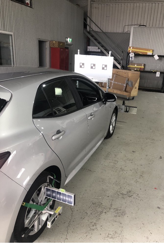 A car in the Cascade Autoglass workshop with the ADAS calibration target board set up in front of it and alignment clamps on the wheels